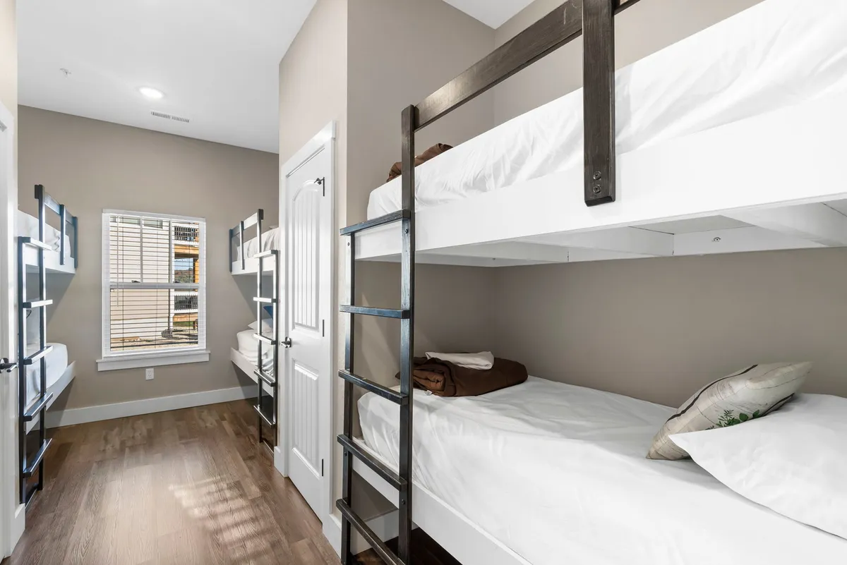 A playful and cozy bunk room with multiple bunk beds, a window letting in natural light, and built-in shelves for storage. The space feels welcoming for children or groups, encouraging bonding and shared experiences.