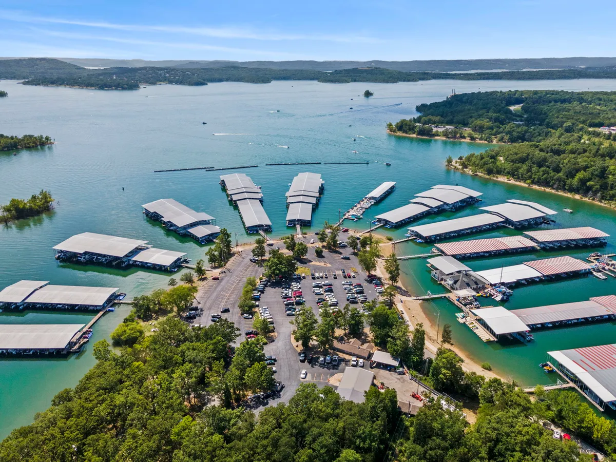 A vibrant lakeside marina scene with several boats docked, surrounded by lush trees and a spacious parking area. The marina is alive with recreational possibilities, inviting visitors to rent boats, fish, or simply enjoy the picturesque views. The overall mood is active and relaxed, perfect for launching a day of lake adventures.