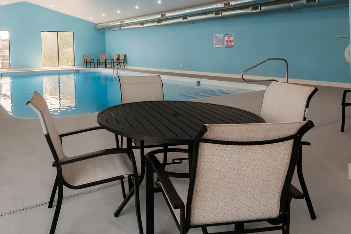 An inviting indoor pool area with seating and expansive windows letting in natural light. The tranquil environment suggests relaxation and year-round swimming opportunities, regardless of the weather outside.
