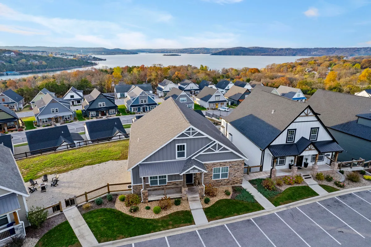 A panoramic exterior shot capturing lake views from the neighborhood, with clustered houses, open landscapes, and accessible parking. The image conveys the ease of walking or biking to the lake, as well as the sense of a friendly, scenic community with space for gatherings and sunset watching.
