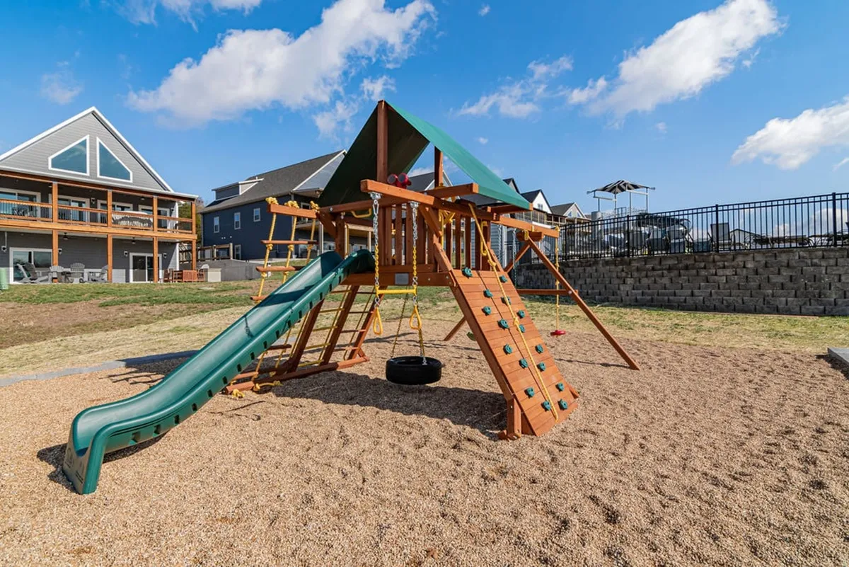 A joyful playground setting with slides, swings (including a tire swing), and a climbing structure nestled among trees. The area is energetic, filled with the promise of children's laughter and family gatherings in a safe outdoor environment.
