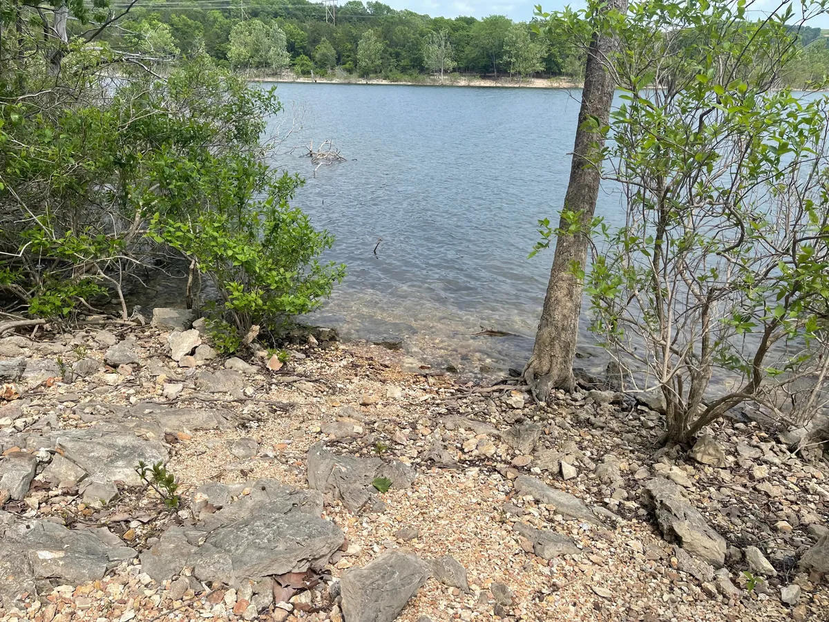 A peaceful lakeshore view featuring calm water, a rocky shore, and rich greenery, all softly illuminated by sunset. The setting encourages fishing, picnicking, hiking, and wildlife spotting, with hidden coves adding a sense of exploration and family-friendly discovery.