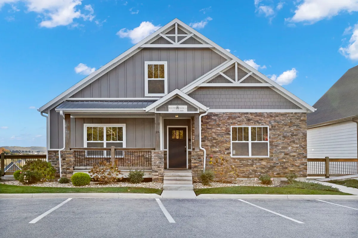 This photo showcases the home's impressive stone façade and inviting front porch, complemented by large windows. The architecture suggests spacious accommodations and modern comfort, hinting at the generous gathering spaces and group-friendly design mentioned in the narrative.