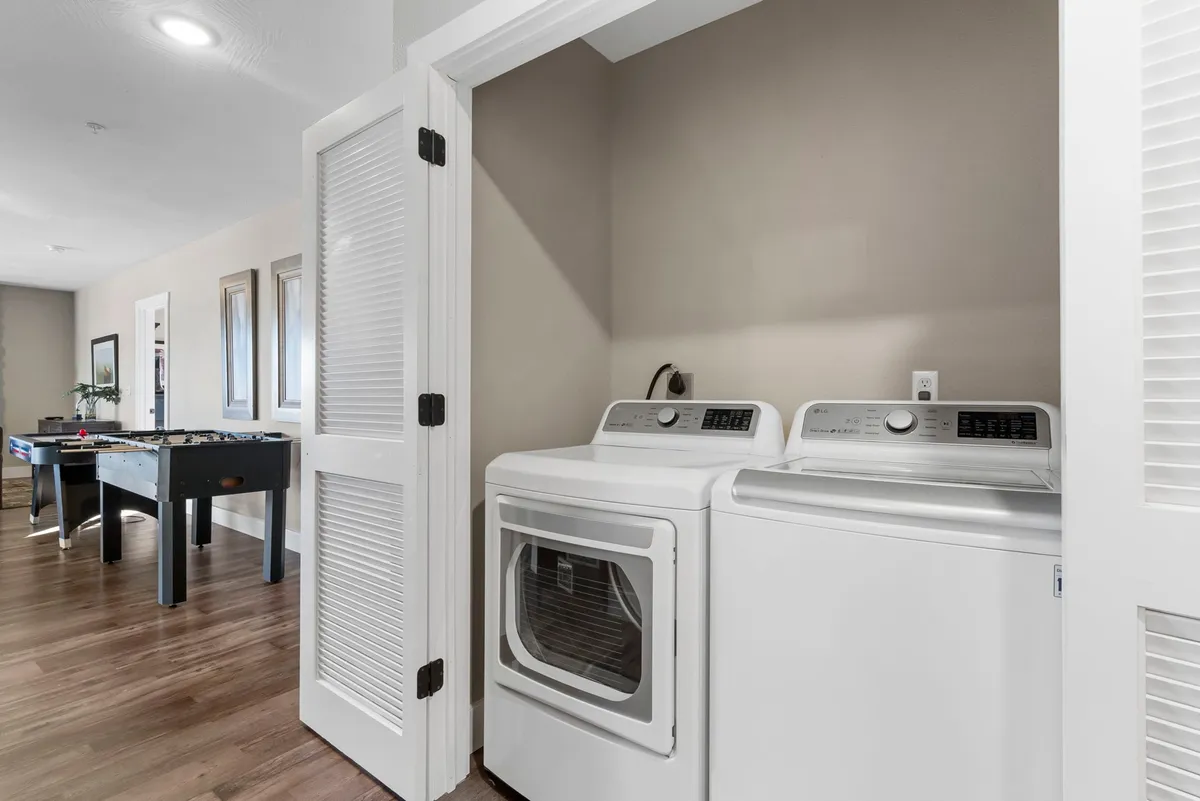 A multi-functional space featuring a foosball table, adjacent to laundry appliances and a doorway leading further into the home, providing a glimpse into recreational options available indoors.
