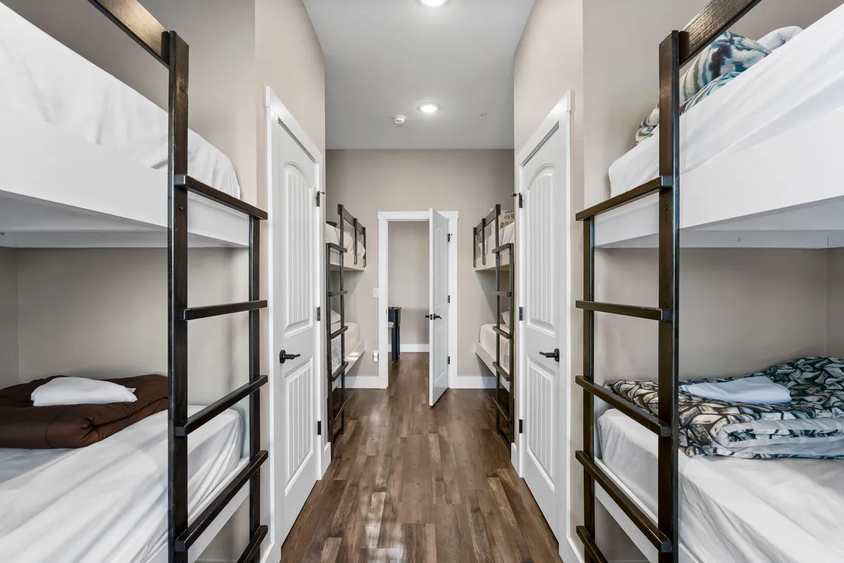 A cozy bunk room with multiple bunk beds, wooden flooring, and an open door leading to another room—perfect for groups of children or cousins sharing stories and adventures.