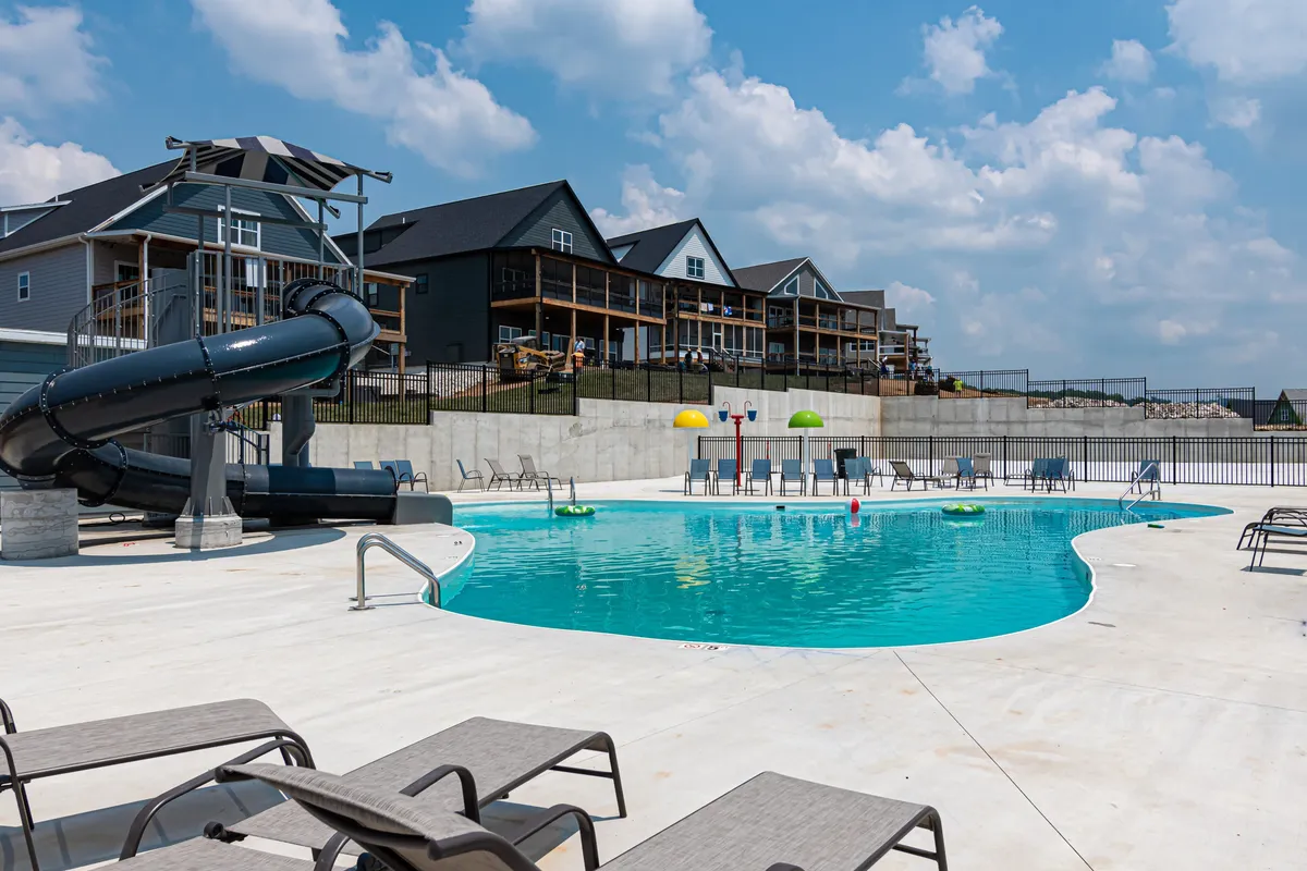 A lively outdoor pool scene featuring a large pool with a water slide, surrounded by lounge chairs and colorful umbrellas. Families and children can be seen playing and sunbathing, creating a joyful and energetic summer atmosphere.
