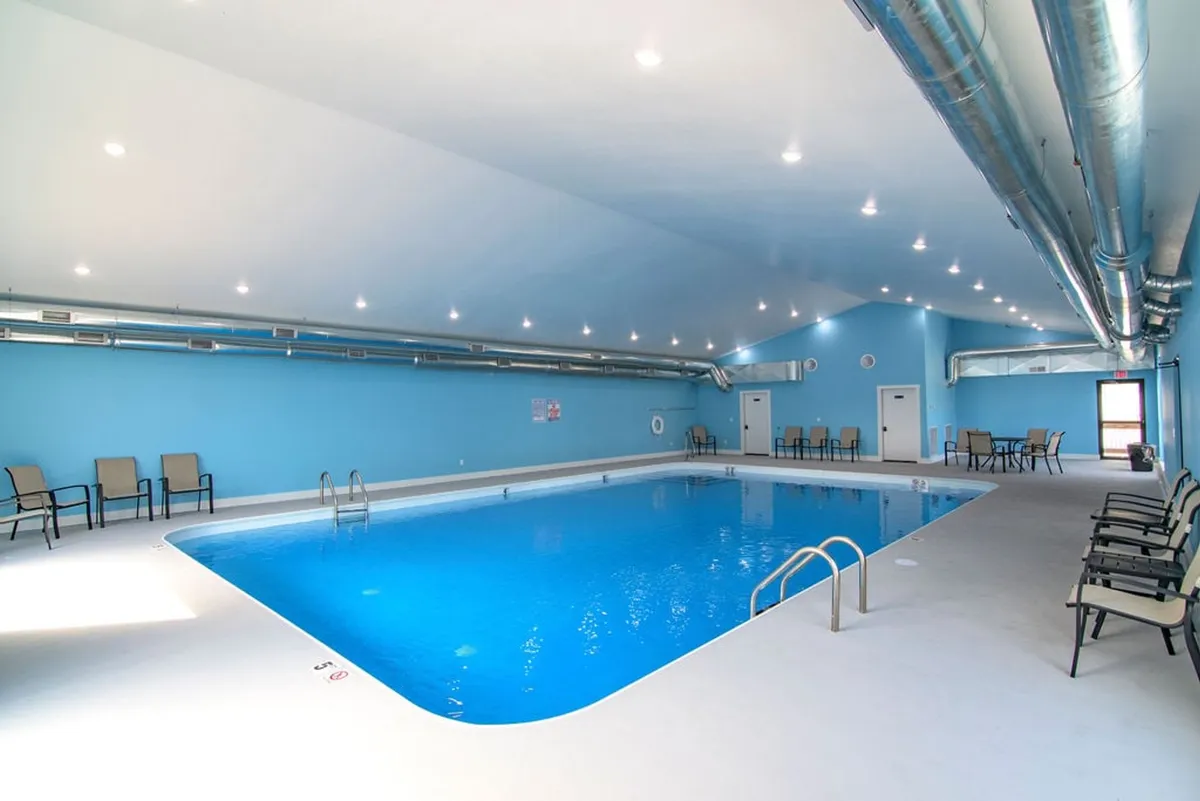 An inviting interior view of the indoor swimming pool, featuring blue walls, a comfortable seating area, and a calm atmosphere. The space is well-lit and designed for relaxation and year-round swimming, regardless of the weather outside.
