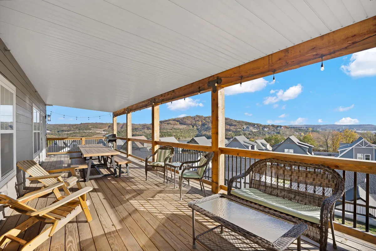 A spacious wooden deck furnished with comfortable outdoor seating, backed by wooden beams and overlooking a breathtaking mountain vista. The deck is elevated, offering clear and uninterrupted views of the natural surroundings, perfect for gatherings or quiet relaxation.